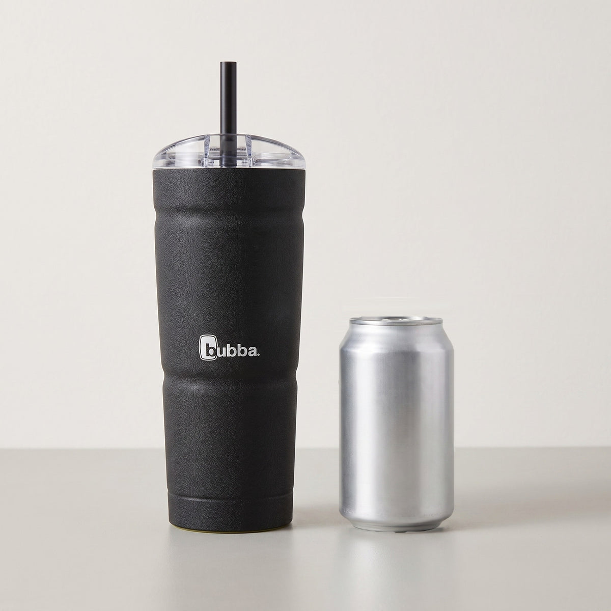 bubba 24 oz Envy S Tumbler in Licorice standing beside a 355 ml can for size comparison. It stands 9 in tall (10.5 in with the straw up).