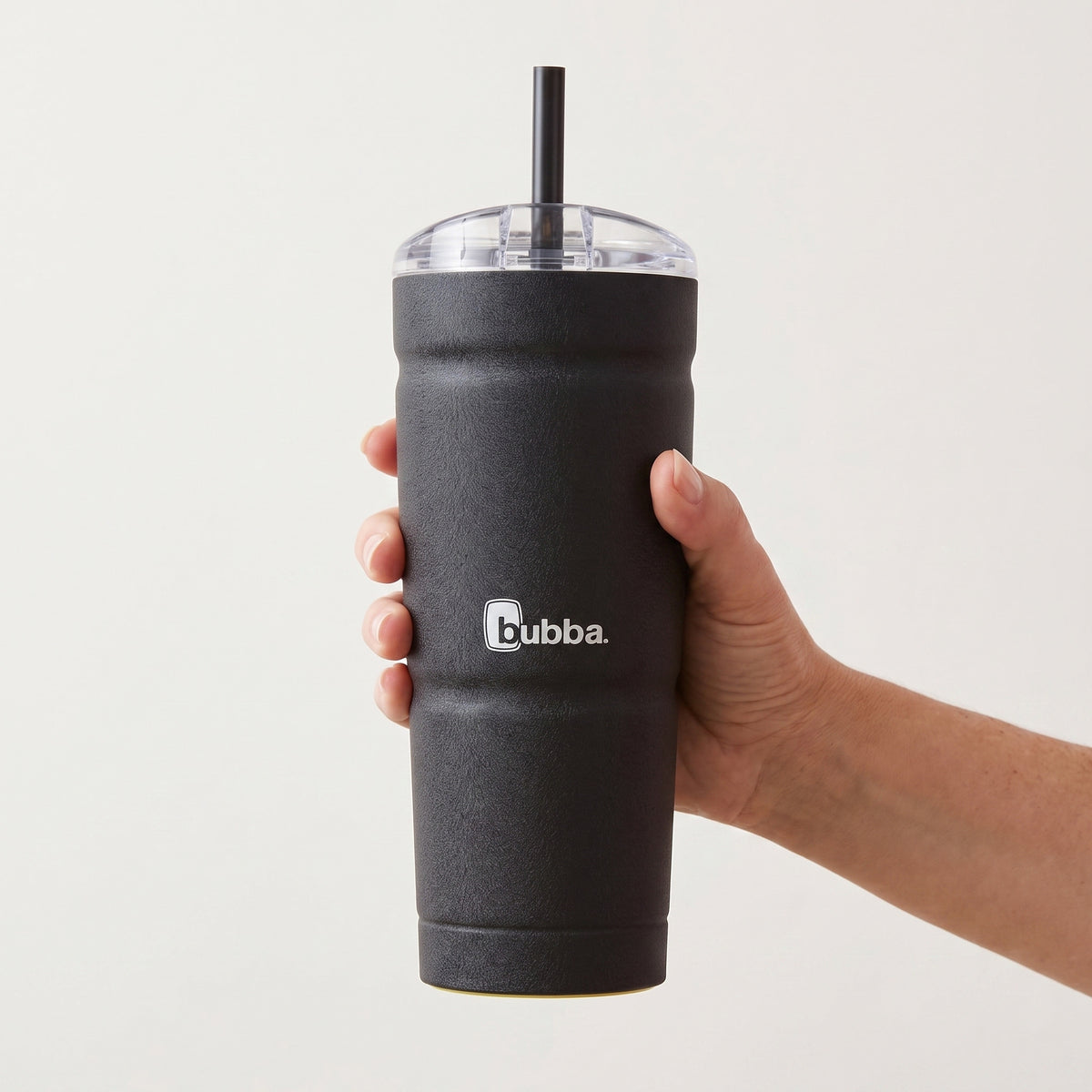 bubba 24 oz Envy S Tumbler in Licorice held in an adult hand, showing its real size. It stands 9 in tall (10.5 in with the straw up).